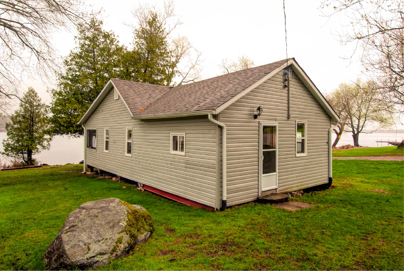 Pigeon Lake Resort Cottage Five, exterior near waterfront with grassy yard, trees, and lake view.